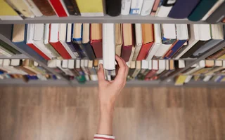 Hand greift Buch aus Regal